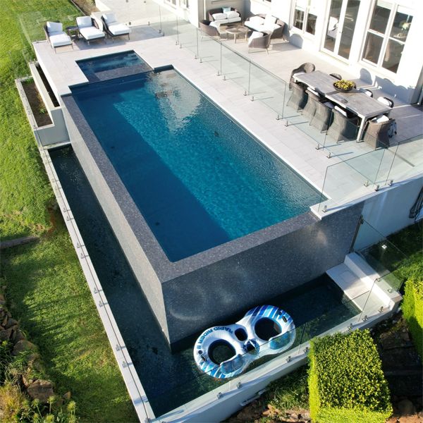 drone view of an infinity pool in a straight lined classic design, with an built-in spa, elevated over a large garden, by Local Pools