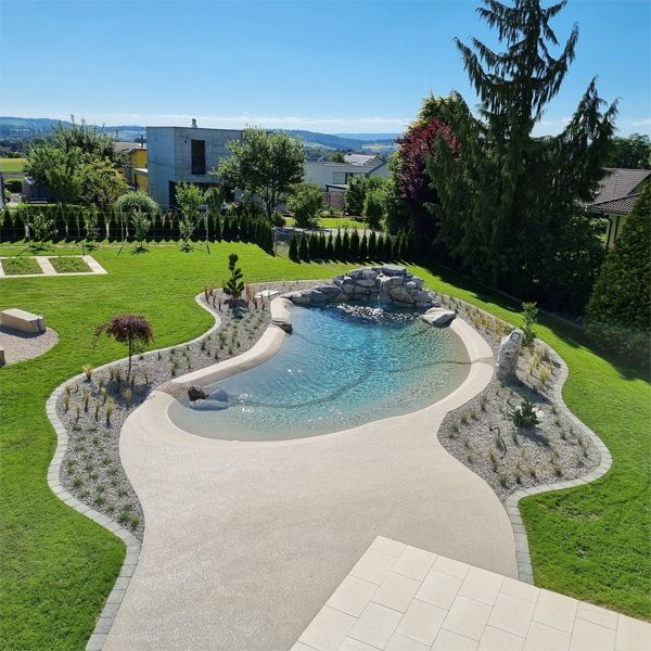 drone view of a custom beach pool, with a waterfall over the rocks, and complete landscaping in a large garden, by Biodesign Pools Deutschland