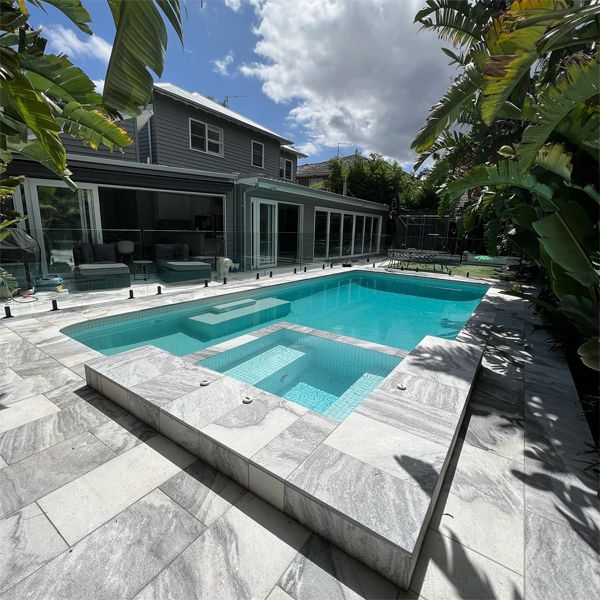 Elegant pool renovation with built-in spa, by Revival Pools, with a combination of coatings; white glass tile and pebbletec, and gray colored exterior stone