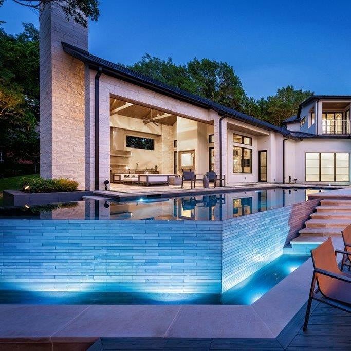 Design infinity pool in straight lines and angles, with dark color coating, by Pool Environments, illuminated at night