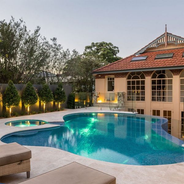 Custom curved infinity pool with built-in spa, by Fluid Design, illuminated at sunset