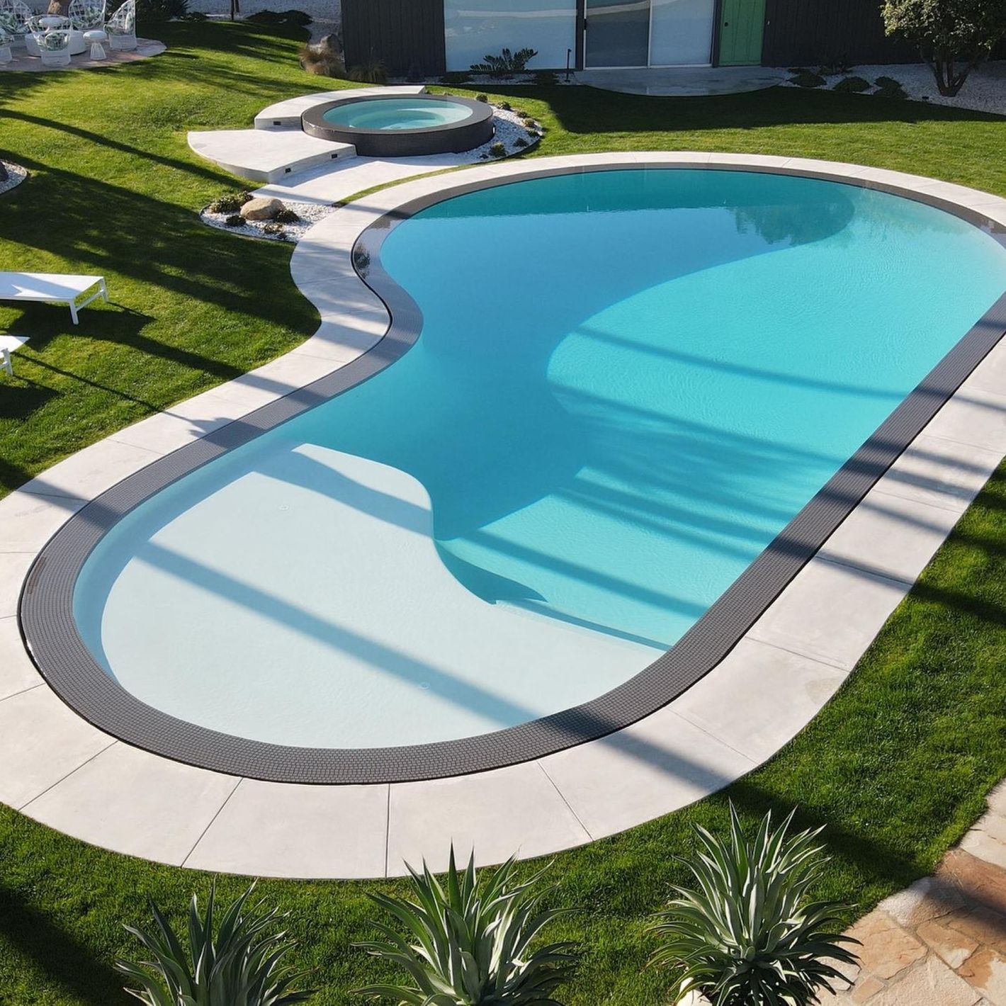 Beautiful overflow pool with kidney-shaped design and independent spa, by MPS Builders, with contrast between the white interior coating and the dark color of the overflowing space