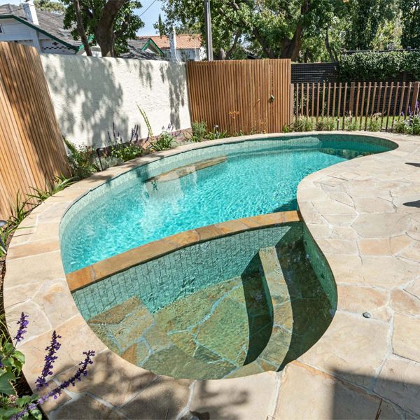 Kidney-shaped pool, with a built-in spa, and a coating that combines glass tile mosaic and stone, by Striking Pools