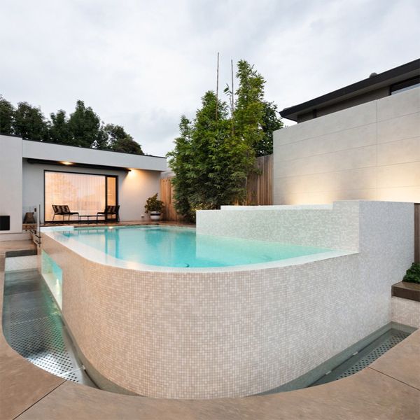 Custom infinity mini pool with a light colored glass mosaic tile coating, by Feature Pools, built above ground in a small backyard