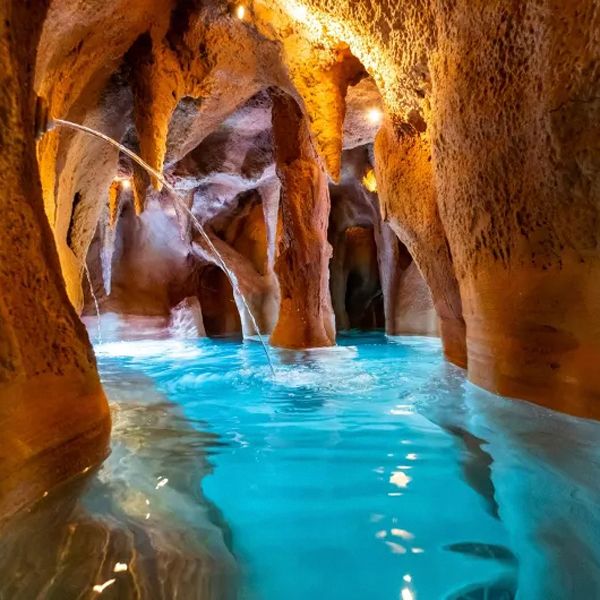 Custom indoor pool, simulating the interior of a cave, with different water features and waterfalls, by Piscines Ondine