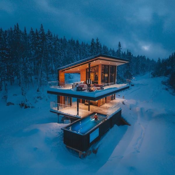 Vue dron at sunset of a mini container pool with a transparent underwater window, by Modpools, in a cabin in the middle of the snowy forest