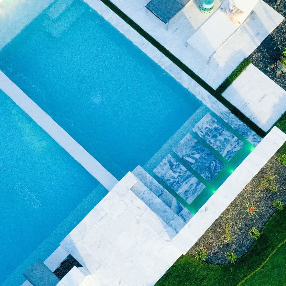 drone view of mini pool with relaxation area, over which another infinity pool overflows, by Hauk Custom Pools