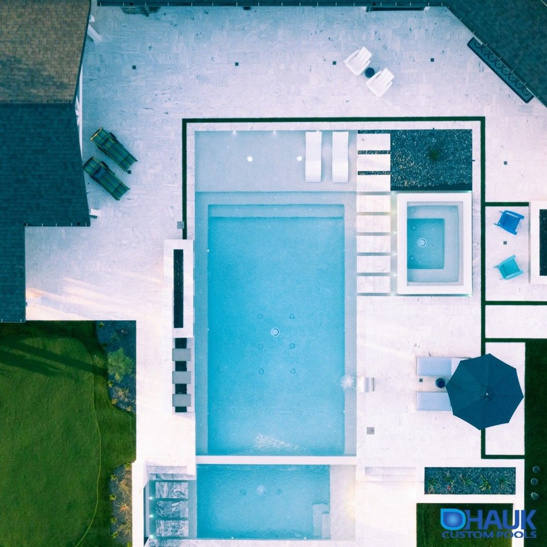 Drone view of a luxury infinity pool, by Hauk Custom Pools, with a geometric design, spa area, relaxation area, water waterfalls