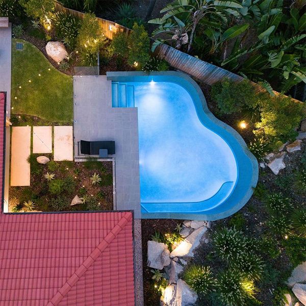 drone view of a small garden with a cool custom pool by Rogers Pools, characterized by its rounded and irregular shapes, and especially by the wall that rises from the very edge of the pool