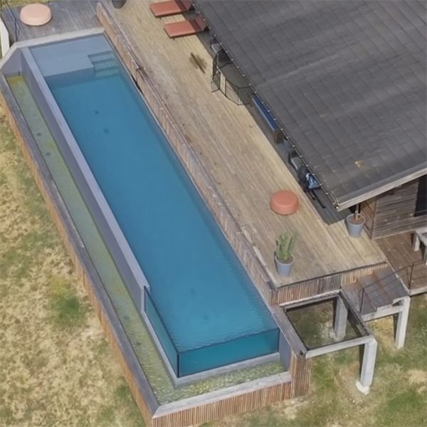 Drone view of an infinity lap pool in a house with a wooden terrace, in a project by Aloha Concepteur Exterieurs