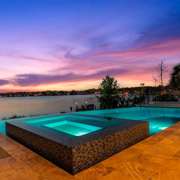 Custom infinity pool with built-in spa, by All Custom Pools, with lake views at sunset