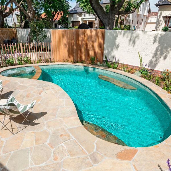 Kidney-shaped private pool, with a built-in spa, and a cladding that combines glass tile mosaic and stone, by Striking Pools