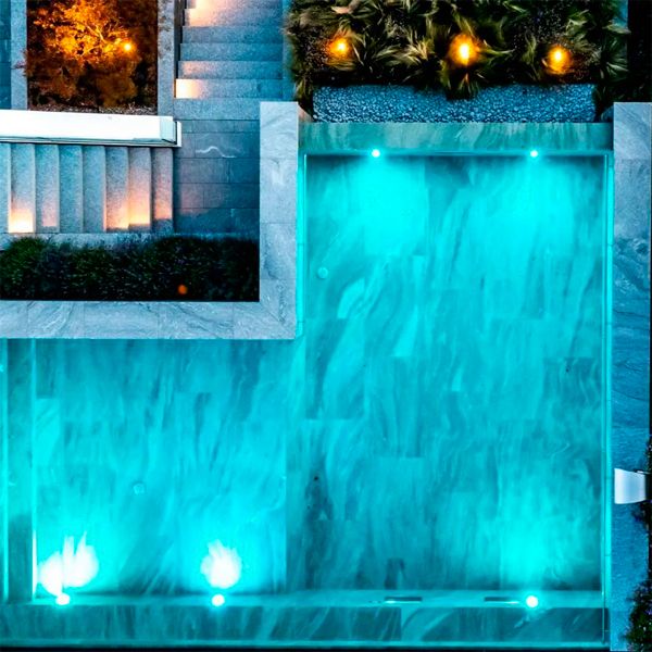 Drone view of bespoke luxury infinity pool, with stainless steel waterfall and spectacular views over the lake, by Vita Bad, illuminated at dusk