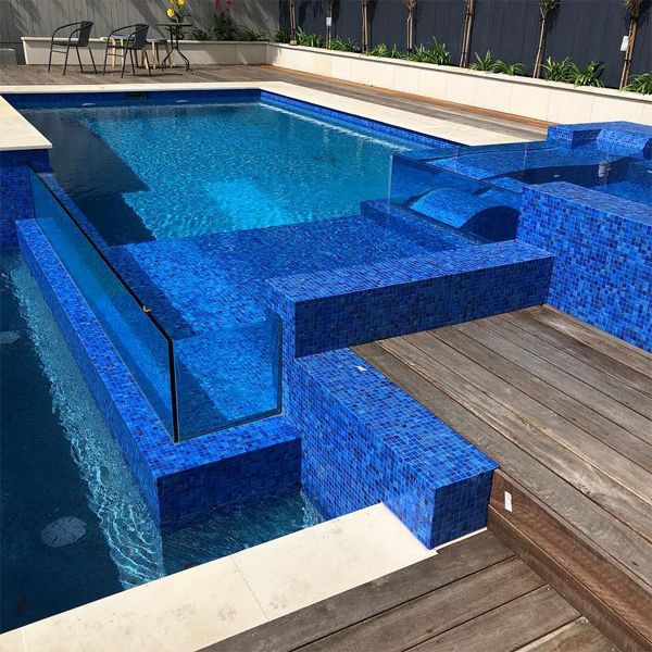 Striking infinity mini pool and spa, with deep blue glass tile coating and transparent walls, by Senator Pools, in a small backyard with wooden decking