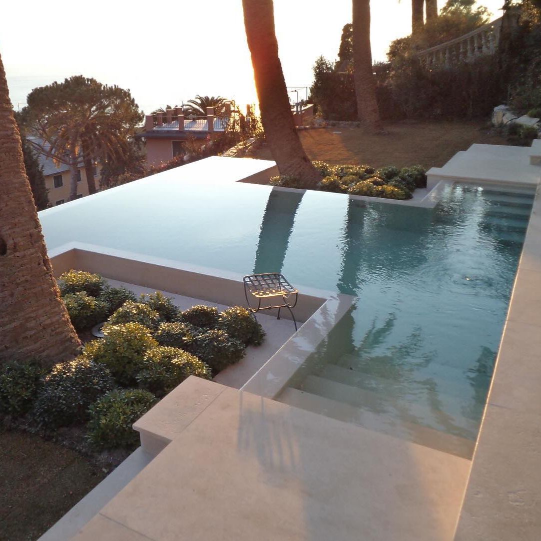 Elegant infinity pool, slightly elevated above the ground, custom design based on straight lines, by Italpool, with a porcelain stoneware cladding, and beautiful views of the sea, at sunset