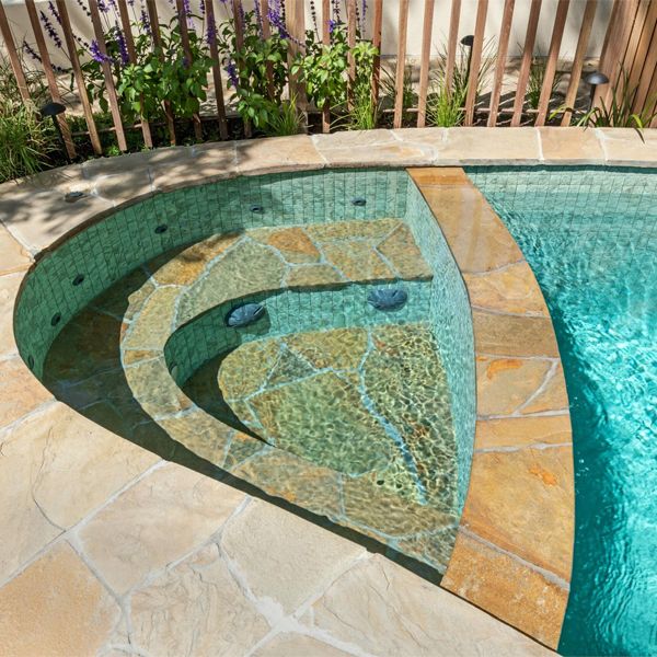 spa inside a custom pool with a coating that combines glass tile mosaic and stone, by Striking Pools
