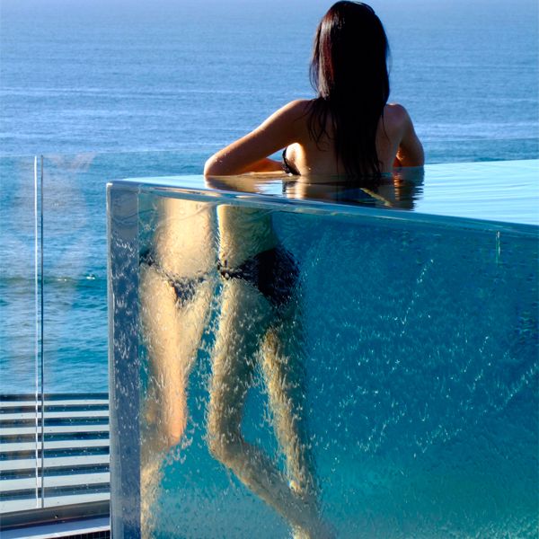 woman looking at the horizon from inside an above ground transparent infinity pool, by Aquatonic Architects