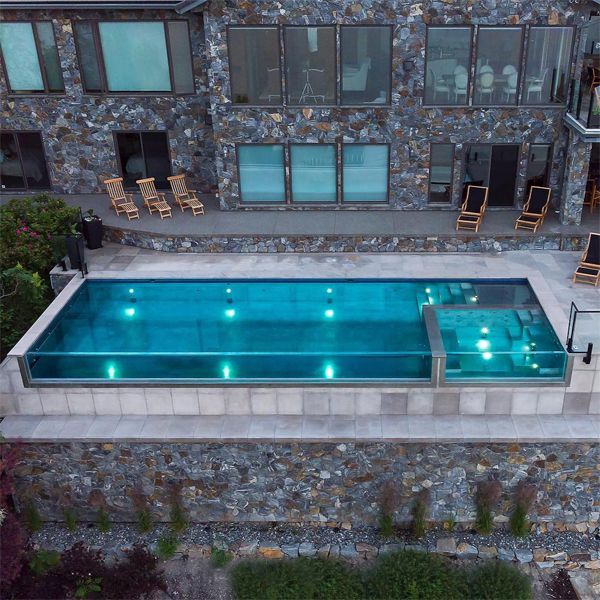 Stainless steel infinity pool with transparent wall and built-in spa, by Valley Pool and Spa, illuminated at sunset