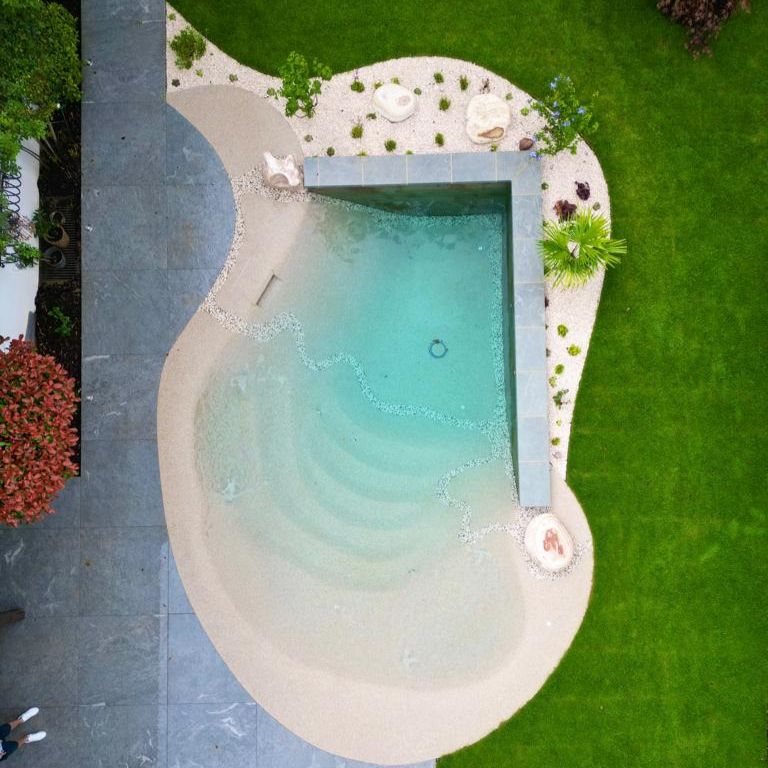 Drone view of a small beach pool, built in a private garden by S&T Creation. The design combines a corner of straight lines with irregular spaces