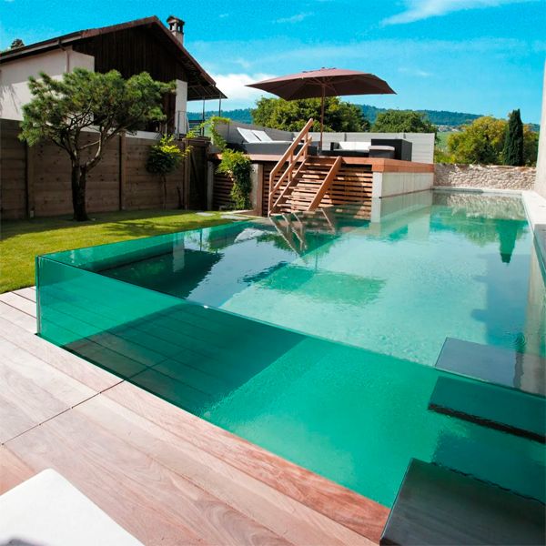 Luxury infinity pool with acrylic transparent walls, in a house with a garden and wooden deck, by Nicollier Group