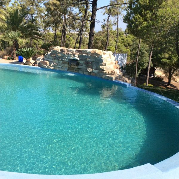 waterfall over decorative rocks in a kidney-shaped infinity pool, by Piscinas Colombinas