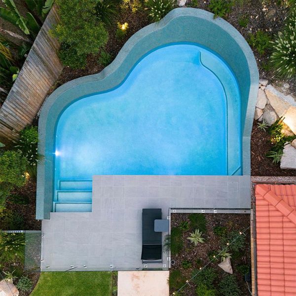 drone view of a custom pool by Rogers Pools, characterized by its rounded and irregular shapes, and especially by the wall that rises from the very edge of the pool, inside a small garden