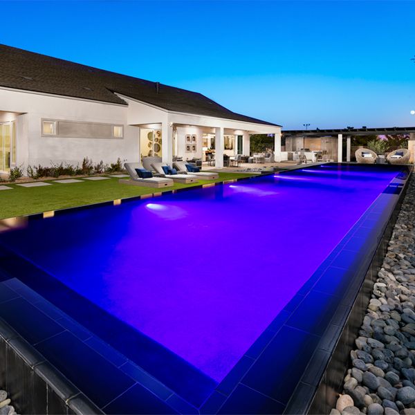 infinity lap pool by Edgewater Custom Pools, lighted at night in a modern house with a large garden