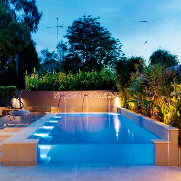 semi-inground private pool with a see-through wall by Jade Pools, lighted at night