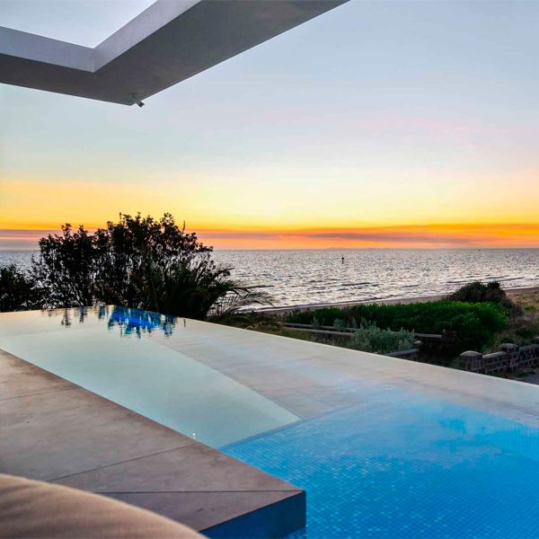 Infinity pool with an underwater window in the floor, at sunset, in a beachside house by Larsen Homes