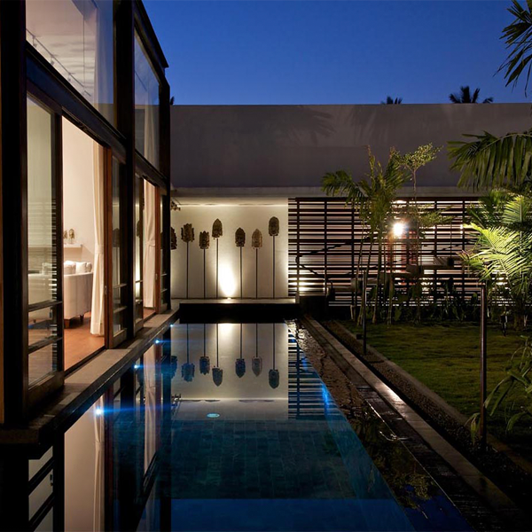 piscina iluminada rodeando vivienda acristalada por la noche