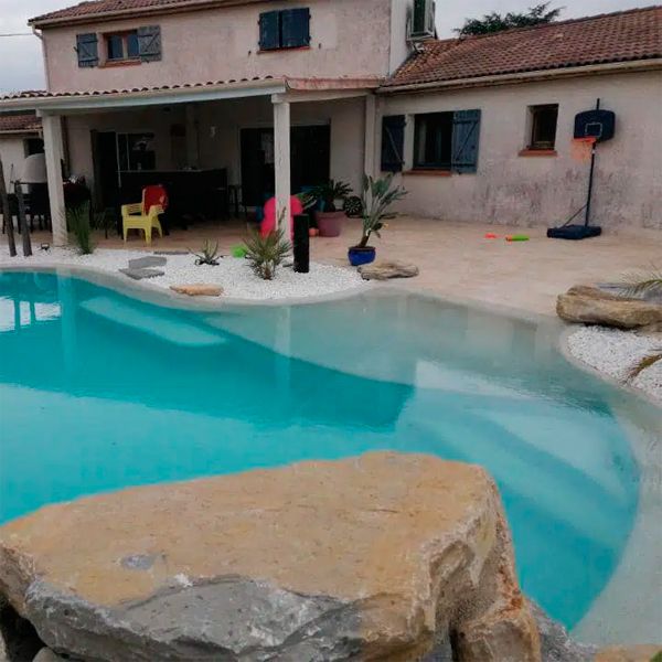 Custom lagoon pool and landscaping in a private garden with many rocks, by Piscines HDP