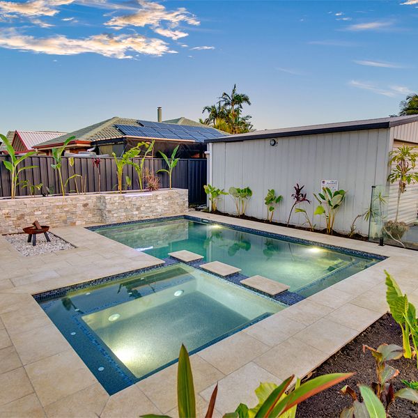 private pool and built-in spa, by Mineral Pools, surrounded by stone pavement in a garden at sunset