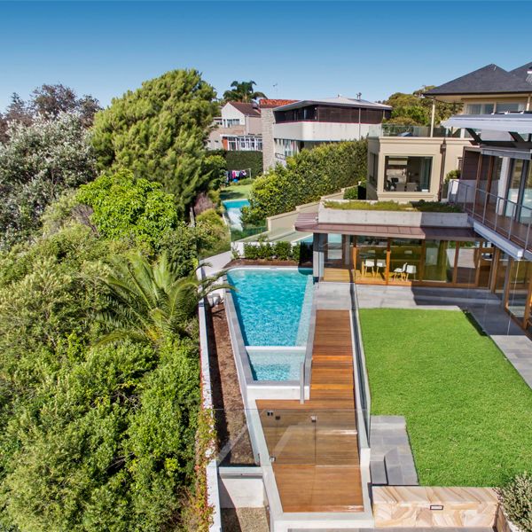 drone view of a custom private pool with a built-in spa, surrounded by wooden deck and garden, in a project by Trademark Pools