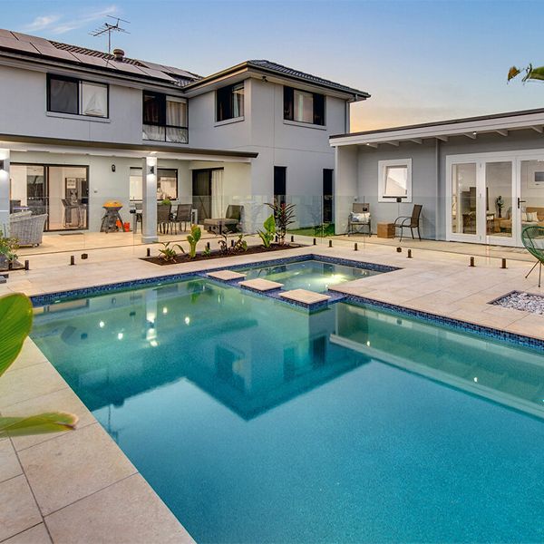 Private custom pool and built-in spa, by Mineral Pools, surrounded by stone pavement in a garden of a house in Manley (Sydney), lighted at sunset