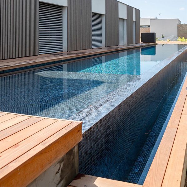infinity lap pool by MCR Piscines and wooden decking in a industrial modern designed space