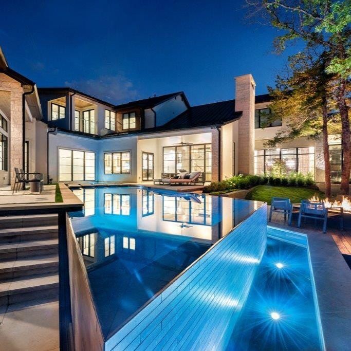 Design infinity pool in straight lines and angles, with dark color coating, by Pool Environments, illuminated at night, in a single-family house