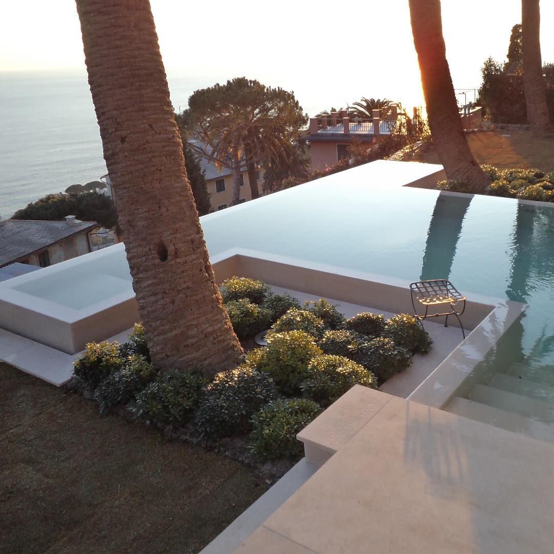 Very elegant infinity pool, slightly elevated above the ground, custom design based on straight lines, by Italpool, with a porcelain stoneware cladding, and beautiful views of the sea, at sunset