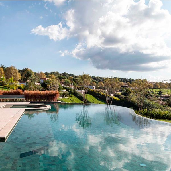 Infinity pool where the clouds of the sky are reflected, in a project by Gilda Meirelles Arquitetura, in the middle of a hill