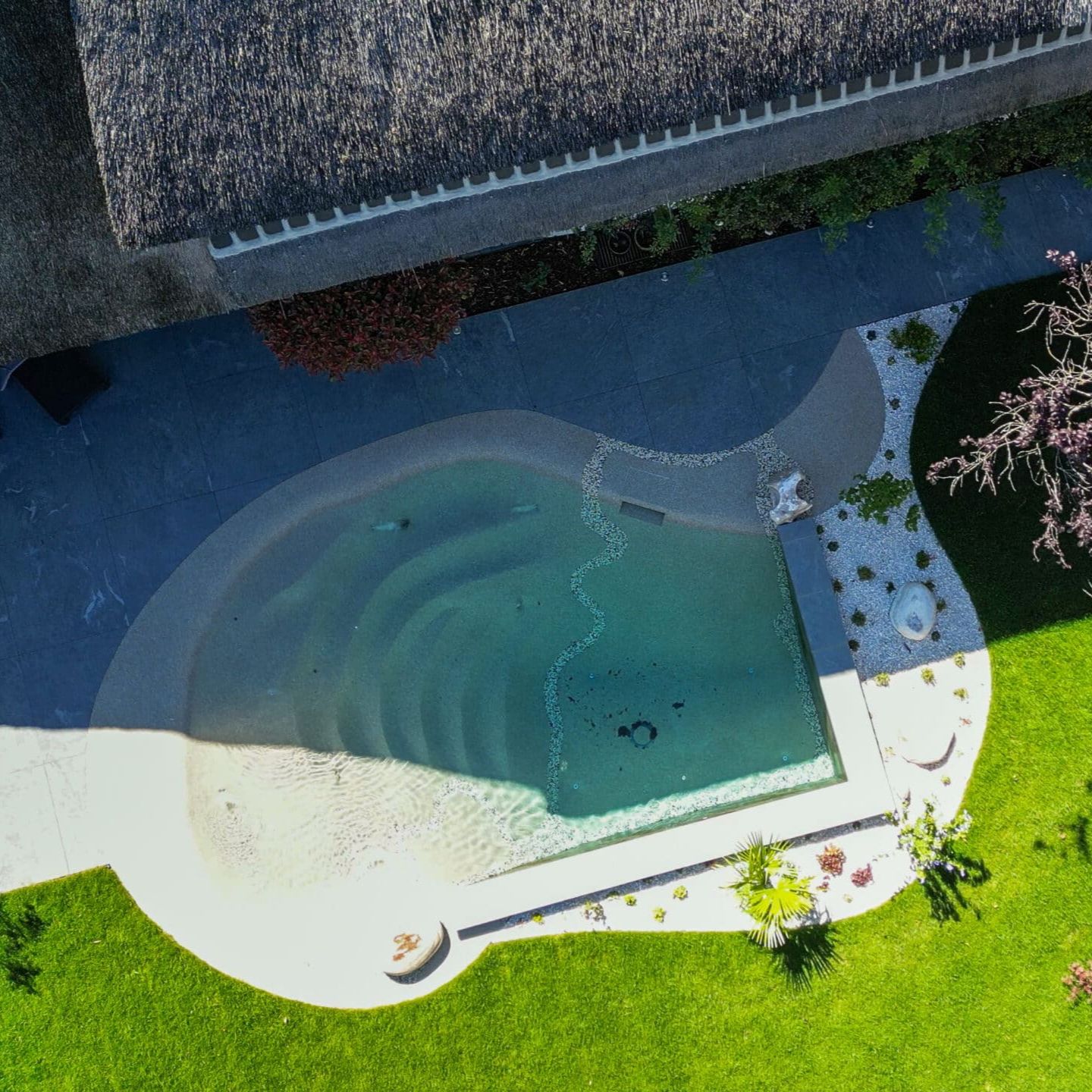 Drone view of a mini beach pool, built in a private garden by S&T Creation. The design combines a corner of straight lines with irregular spaces