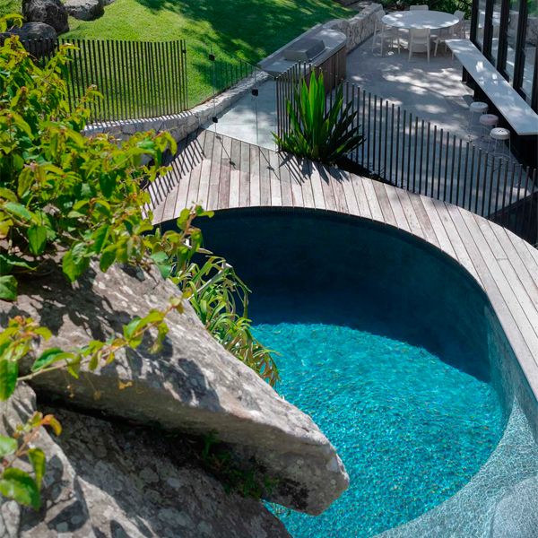 pool surrounded by wooden decking in a lush garden, by Secret Gardens
