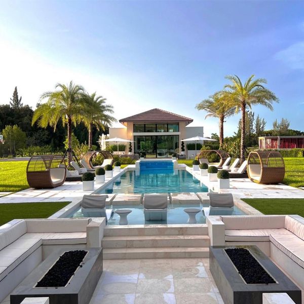custom luxury pool with raised overflow spa, separated by a transparent window, by Custom Pool Systems, in a modern garden with palm trees, hammocks, balinese beds
