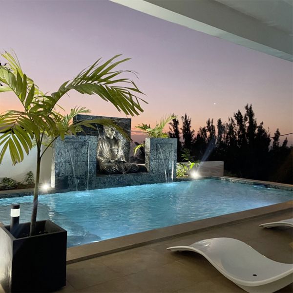 Zen design private mini pool with waterfalls, by Sarana Pools, decorated with a figure of Buddha, and a natural stone coating, lighted at night