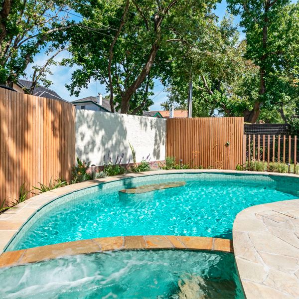 custom private pool, with a built-in spa, and a cladding that combines glass tile mosaic and stone, by Striking Pools