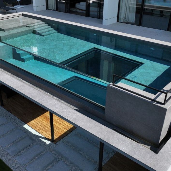 Drone view of a luxurious transparent pool, rectangular designed, with a square-shaped underwater window by Holland Aqua Sight, at the bottom of the pool