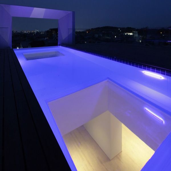 Infinity pool with windows on the floor, illuminated at night, located on the rooftop of a modernist house project by Eastern Design Office