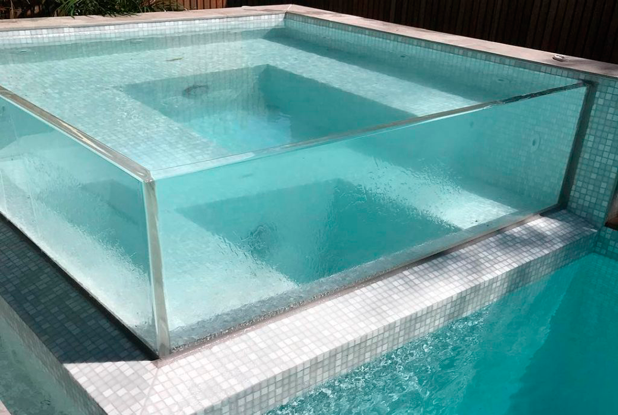 overflowing transparent wall spa over gray tile pool as one of the latest pool trends