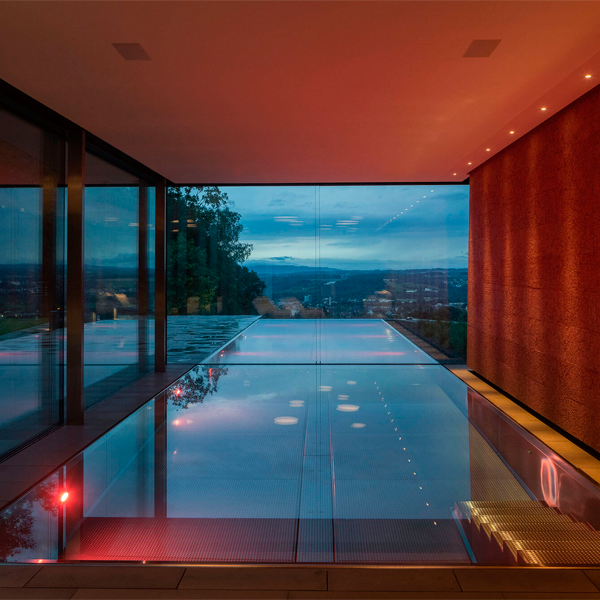 piscina desbordante en acero inoxidable iluminada por la noche, de Bergmann Schwimmbad