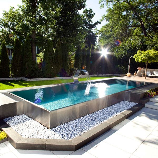Piscina desbordante en acero inoxidable con cascada, también en acero, por Berndorf Pools, en un jardín moderno y minimalista