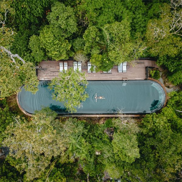 Vista dron de piscina infinita en acero inoxidable, de diesño curvado, situada en medio de la jungla, dentro de un proyecto de hotel de Bill Bensley Architects