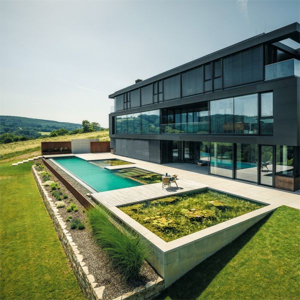 Vista dron de piscina natural con desbordante infinito y estilo canal de natación, de Biotop, en casa de diseño moderno y minimalista